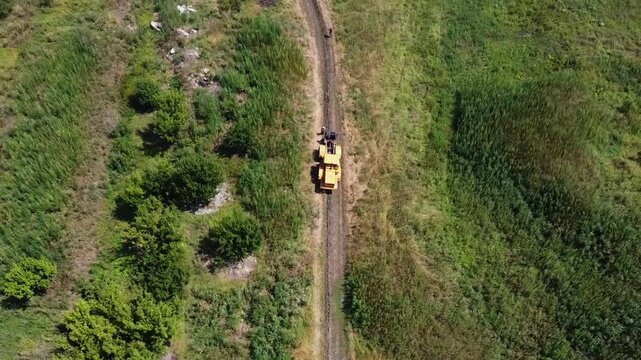 Aerial view of tractor with a cable drum laying fiber optic hawser at countryside. Workers guiding and adjusting rope to ensure proper placement under ground for communication or power infrastructure