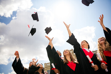 Young graduates celebrate with joy throwing mortarboards into the sky on a sunny day, marking the...
