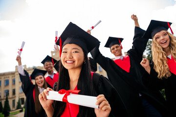 Joyful group of young graduates celebrating their achievement on a bright summer day at the...