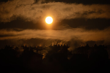 Dramatic sunset with rising chimney smoke over silhouetted village rooftops