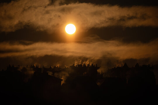 Dramatic sunset with rising chimney smoke over silhouetted village rooftops