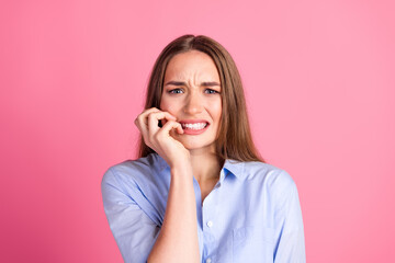 Fototapeta premium Young woman with long brown hair wearing a casual blue shirt showing a worried expression against a pink background