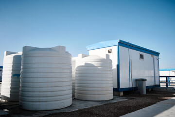 White plastic water tanks stand next to prefabricated industrial building. Newly built single storey prefabricated industrial building. Prefabricated office container building at construction site