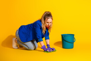 Young stylish woman cleaning floor in vibrant yellow interior with a blue bucket