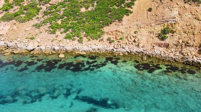 An aerial view of the crystal-clear waters at El Gliaa in Bizerte. The vibrant green hues and gentle waves create a serene and inviting scene for beachgoers.