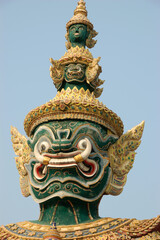 Colorful green and gold giant guardian statue at a Thai temple in Bangkok, standing in front of ornate buildings with a clear sky background