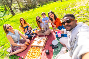 Group of friends enjoying pizza picnic and taking a selfie in park