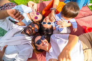 Happy friends lying on blanket taking selfie with baby