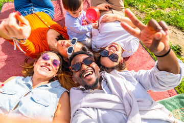 Happy friends taking a selfie while lying on a blanket in a park