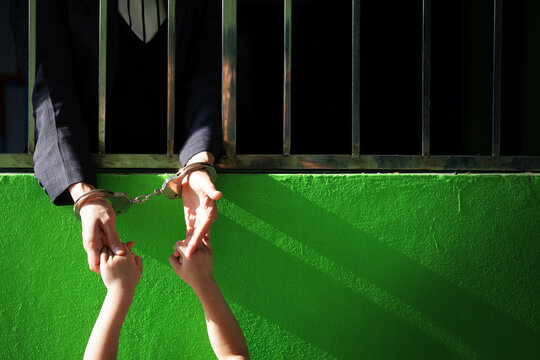 Arrested Individual Reaching Hand to Child Through Prison Bars