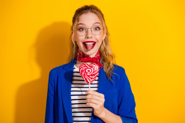 Cheerful young woman holding a heart-shaped candy in front of a vibrant yellow background