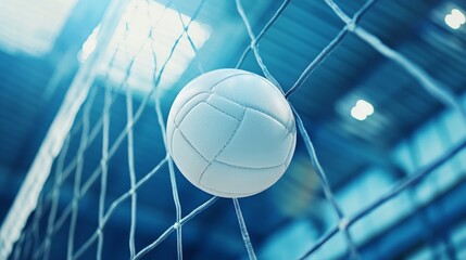 Low-angle close-up of a white leather volleyball soaring over the net in an indoor volleyball arena during a competitive match, capturing the fast-paced action and intensity of the game.


