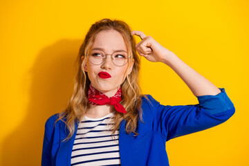 Trendy young woman in blue attire posing with thoughtful expression against bright yellow background