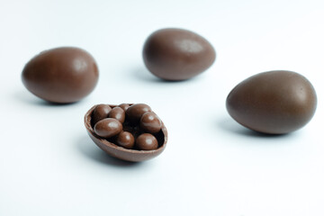A group of chocolate Easter eggs, one of them broken open to reveal small chocolate candies inside, set against a clean white background. A perfect festive treat for Easter celebrations.
