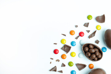 A broken chocolate Easter egg with candy-coated chocolates spilling out, scattered on a white background. A festive and playful composition perfect for Easter celebrations and sweets-themed designs.