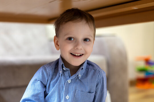 Happy young boy playing under a table. A cheerful young boy in a blue shirt smiles while playing under a table at home, enjoying a fun and playful moment.