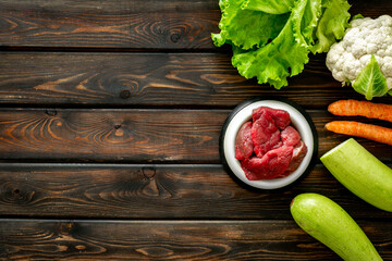 Natural pet food in feeding bowl and ingredients meat and vegetables, top view
