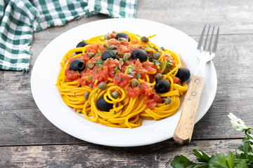 Italian Pasta puttanesca with tomato sauce, capers, and black olives on wooden table