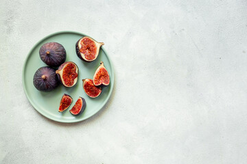 Plate with fresh ripe figs whole and slices with green leaves on white background. Top view