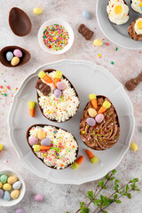Easter dessert. Chocolate eggs with cheesecake filling decorated with chocolate candies and sugar sprinkles on a white plate on gray concrete background. Copy space.