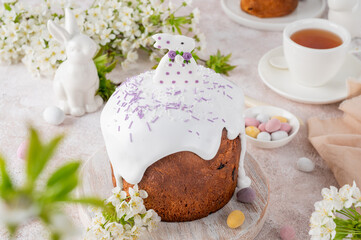 Easter sweet bread or Easter cake - Paska with sugar glaze, colored sprinkles and sugar bunny on top on a wooden board on a concrete background. Copy space.