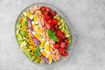 Salmon salad with avocado, boiled eggs, sweet corn, tomatoes, lettuce and red onion on concrete background. Healthy food. Top view.