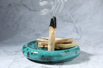 Palo Santo stick smoldering on grey table, closeup