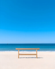 Obraz premium Serene beach scene with a lone wooden bench facing the ocean under a vibrant blue sky