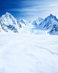 Vast, snow-covered valley nestled between towering, glacier-capped mountains under a vibrant blue sky