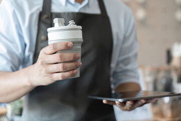 Sustainable Practices and Coffee Culture. A barista holding a reusable cup while showcasing ecofriendly coffee options in a cafe environment.