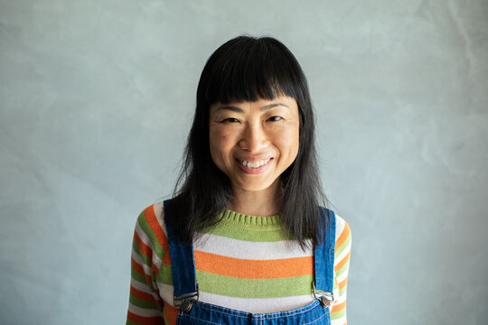 Portrait of a cheerful Asian woman wearing striped sweater and denim overalls