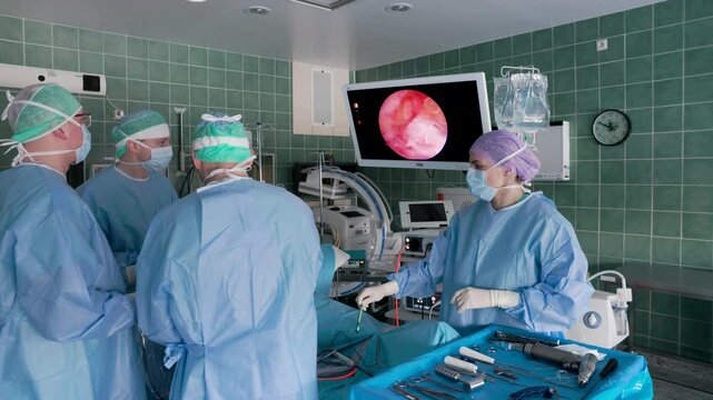 A team of surgeons in sterile gowns performs an endoscopic procedure in an operating room, using advanced medical imaging technology to guide the operation