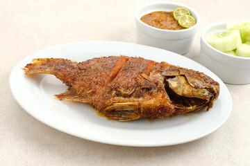 Grilled Tilapia with honey and soy sauce or Ikan Nila Bakar. Served on white plate with sambal (chilli sauce) and cucumber
