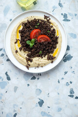 Hummus with roasted ground beef on a white and blue granite background, vertical shot with copy space, top view