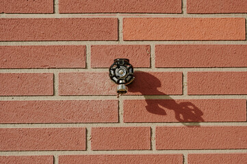 Outdoor faucet attached to red brick wall creating functional yet visually appealing design...