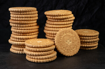 Stacks of round, golden-brown biscuits with a textured edge, arranged on a dark surface, creating a rustic and inviting bakery-style presentation