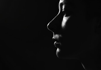 Black and white profile revealing elegant Asian woman silhouetted with dramatic rim lighting, casting shadowy contemplative mood against deep monochromatic background © Rohit k 