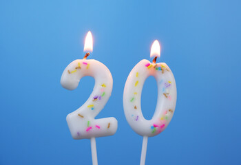 Burning white birthday candles on blue background, number 20.