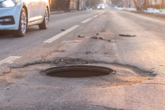 An open manhole on the road and a car driving dangerously close to it