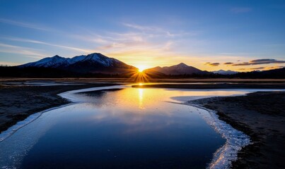 Obraz premium Sunrise paints the sky with golden hues over the mountains, reflected in the calm lake.