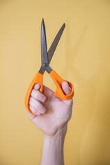 hand holding pair of scissors on yellow background