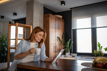 Smiling woman enjoying coffee and using digital tablet in modern kitchen