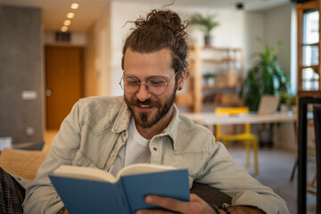 Smiling freelancer reading a book at home office: comfortable and productive workday