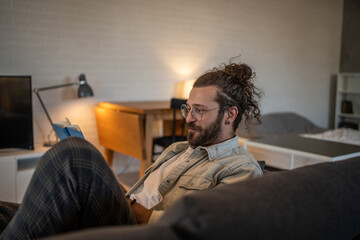 Obraz premium Man reading a book while relaxing on sofa at home