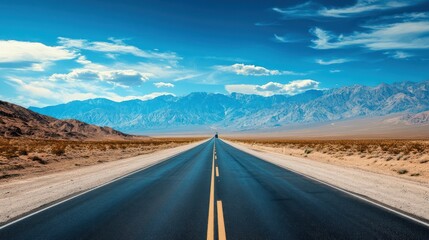 Naklejka premium Open road through desert landscape leading to mountains under a blue sky.