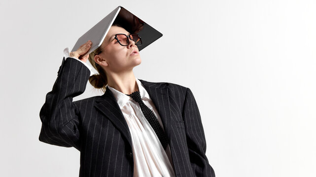 Portrait of confident woman in modern business outfit using laptop as unconventional prop against white background. Concept of business, digital transformation, creative thinking, adaptability.