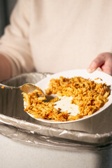 Vertical image of woman holding white plate with food leftovers and throwing away food into garbage bin trash. Compost from leftover food. Environmentally responsible, reducing pollution.