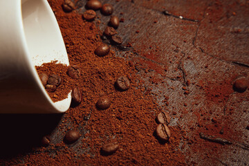 Beans and ground fresh coffee on a dark background crumbled mess and inverted part of a white cup