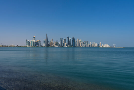 View of modern skyline with skyscrapers reflecting on water under blue sky, Al Souq, Doha, Qatar.