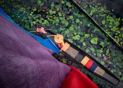 Inle Lake, Myanmar - 14 November 2019: View of mother and child in a boat drying colorful cloth on water with lilypads, Inle Lake, Shan State, Myanmar.